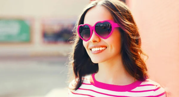 美しいです幸せな笑顔若いですブルネット女性で赤ハート形のサングラス上のピンクの背景 — ストック写真