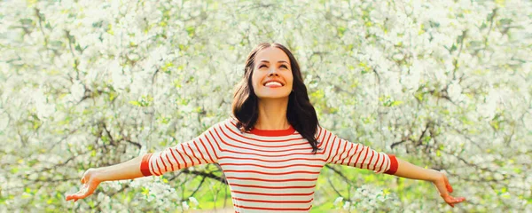 幸せな笑顔若い女性彼女の手を上げて春に咲く庭で花の背景 ストック写真