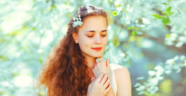 白い花の背景に春の庭に長い巻き毛の美しいかわいい若い女性の肖像画 — ストック写真