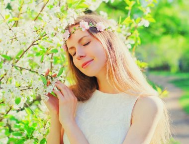 Güzel, genç bir kadının portresi ve çiçek yaprakları. Çiçek açan bahçede çiçek bandı takan beyaz ağaç.