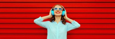 Renkli kırmızı arka planda kulaklıkla müzik dinleyen mutlu, gülümseyen genç bir kadının portresi.