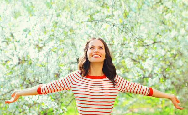 幸せな笑顔若い女性彼女の手を上げて春に咲く庭で花の背景 — ストック写真