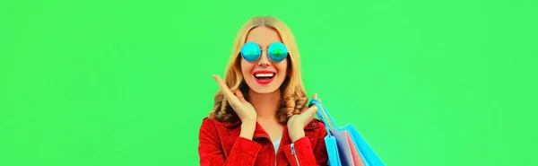 スタイリッシュで幸せな笑顔の若い女性のカラフルな肖像画でショッピングバッグポーズを身に着けている赤いジャケット緑の背景 — ストック写真