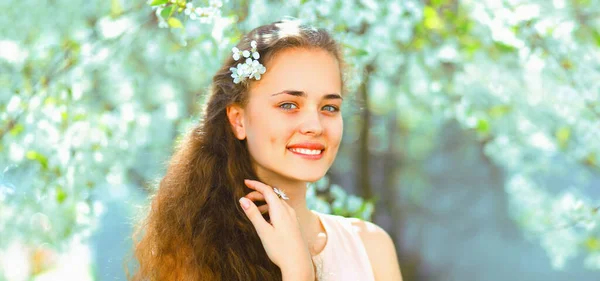白い花の背景に春の庭に長い巻き毛の美しいかわいい笑顔の若い女性の肖像画 ストック写真
