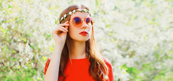美丽的年轻女子的画像 头戴花环 戴着墨镜 挂在春花绽放的花园背景上 — 图库照片