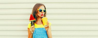 Genç bir kadının yaz portresi taze meyve suyu içerken dondurma şeklinde bir karpuz dilimi ya da beyaz arka planda lolipop çubuğu, reklam metni için boş fotokopi alanı.