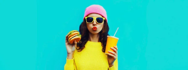 ブルガーとジュースのカップを持つスタイリッシュな若い女性の肖像 高速食品の青のカラフルな背景に — ストック写真