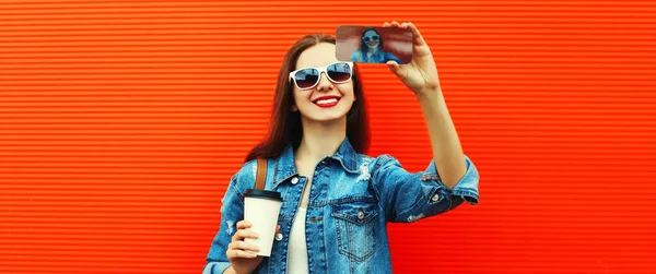 幸せな笑顔の若い女性の肖像写真でスマートフォンで撮影バックパックで赤の背景 ロイヤリティフリーのストック写真