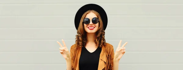 黒丸の帽子を身に着けている美しい若い笑顔の女性の肖像画 グレーの背景に茶色のジャケット — ストック写真