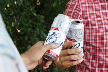 KHARKIV, UKRAINE - 1 Ağustos 2021: iki adam doğada Budweiser Alkol Birası kutularını tutuyor. Budweiser, Amerika 'nın en popüler Anheuser-Busch Inbev markası..