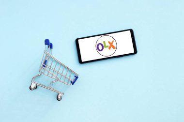 KHARKIV, UKRAINE - NOVEMBER 12.2020: Akıllı telefonlu alışveriş arabası mavi arka planda OLX logosu açtı.