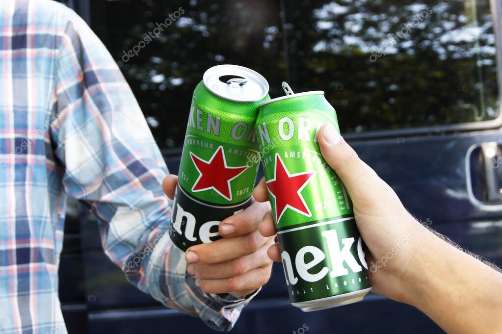 KHARKIV, UKRAINE - AUGUST 1, 2021: Two guys are holding cans of Heineken alcoholic beer in nature. Heineken is a Dutch brewing company, the largest in the country and the second largest in the world.
