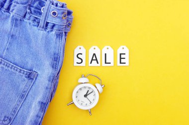Düz yatak, kot pantolonlar, beyaz etiketler ve sarı arka planda indirimler. Alışveriş ve indirim konsepti. Kara Cuma.