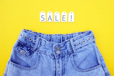 Düz yatış, beyaz etiketli kot pantolonlar ve sarı arka planda yazıt satışı. Alışveriş ve indirim konsepti. Kara Cuma.