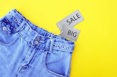 Düz yatış, gri etiketli kot pantolonun ayrıntıları ve sarı arka planda BIG satışı. Alışveriş ve indirim konsepti. Kara Cuma.