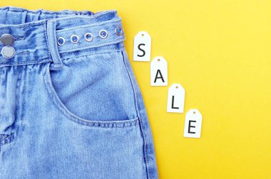 Düz yatış, kot pantolonlar, beyaz etiketler ve sarı arka plandaki yazıt satışı. Alışveriş ve indirim konsepti. Kara Cuma.