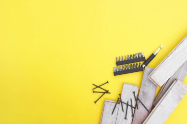 Kendi kendine dokunan vidalar, birkaç parça ve sarı arka planda tahta tahtalar. Metne yer var..