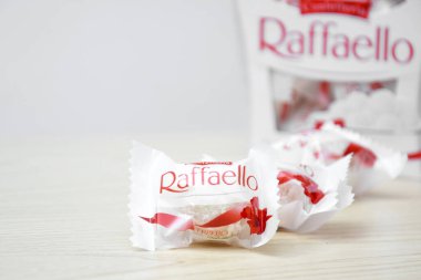KHARKIV, UKRAINE - 23 Ekim 2021: Raffaello tatlılar açık ahşap bir masa ve beyaz zemin üzerinde. Raffaello küresel bir Hindistan cevizli badem şekerlemesidir..