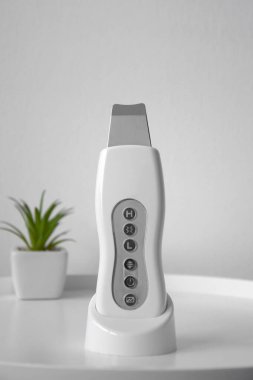 Deriyi soymak ve beyaz bir masadaki gözenekleri temizlemek için ultrasonik temizleyici. Bulanık yeşil bir çiçeğin arka planında. Güzellik konsepti.