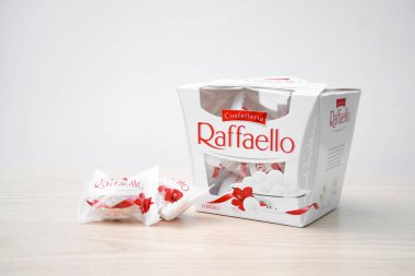 KHARKIV, UKRAINE - 23 Ekim 2021: Raffaello tatlılar açık ahşap bir masa ve beyaz zemin üzerinde. Raffaello küresel bir Hindistan cevizli badem şekerlemesidir..