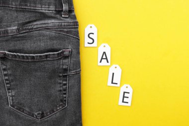 Düz yatış, siyah kot, beyaz etiketler ve sarı arka planda indirim. Alışveriş ve indirim konsepti. Kara Cuma.