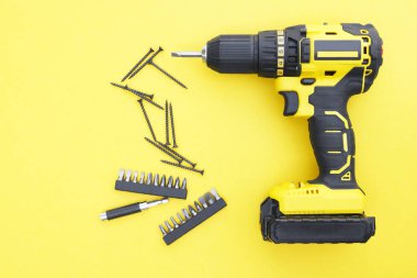 Sarı arka planda sarı-siyah tornavida, vidalar, birkaç parça. Üst görünüm.