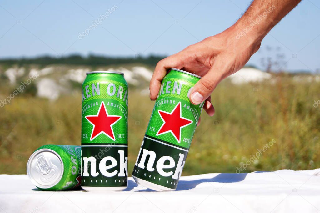 KHARKIV, UKRAINE - AUGUST 1, 2021: Many cans of Heineken alcoholic beer lie against the backdrop of the landscape. Heineken is a Dutch brewing company, the largest in the country and the second largest in the world.