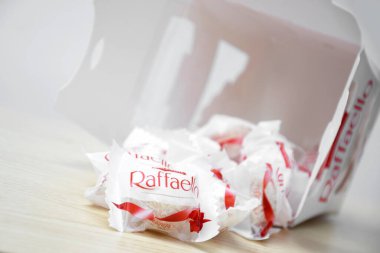 KHARKIV, UKRAINE - 23 Ekim 2021: Raffaello tatlılar açık ahşap bir masa ve beyaz zemin üzerinde. Raffaello küresel bir Hindistan cevizli badem şekerlemesidir..