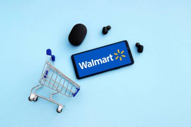 KHARKIV, UKRAINE - NOVEMBER 12.2020: Akıllı telefonlu alışveriş arabası mavi arka planda Walmart logosu açtı.