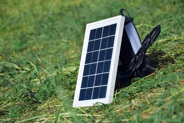Small compact solar battery for tourism. She is charging while lying on the green grass.