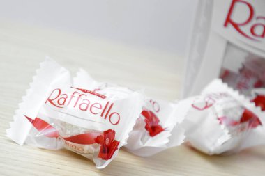 KHARKIV, UKRAINE - 23 Ekim 2021: Raffaello tatlılar açık ahşap bir masa ve beyaz zemin üzerinde. Raffaello küresel bir Hindistan cevizli badem şekerlemesidir..