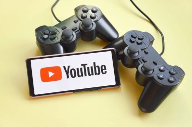 Kharkiv, Ukrayna - 20 Şubat 2021: YouTube ekranlı akıllı telefon ve sarı arka planda iki oyun joystick 'i. Minimalizm. Siber spor konsepti. Akıyor.