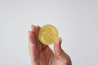Kız elinde hafif bir arka planda altın bir bitcoin tutuyor. Dijital para ve bitcoin değişim konsepti.