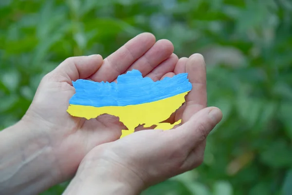 A woman holds in her hands the outline of the country of Ukraine, decorated in blue and yellow, like the national flag of Ukraine. Independence, flag, Constitution Day. War in Ukraine.