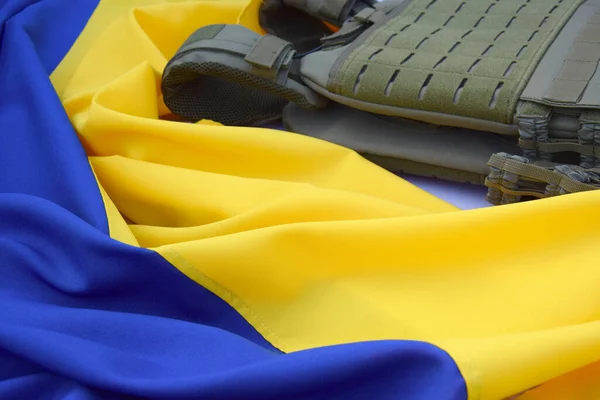 Tactical, military body armor with plates on the background of the flag of Ukraine. The concept of protecting the body from shots in the war in Ukraine.