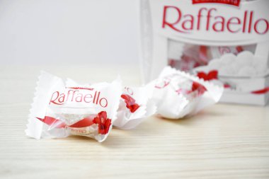 KHARKIV, UKRAINE - 23 Ekim 2021: Raffaello tatlılar açık ahşap bir masa ve beyaz zemin üzerinde. Raffaello küresel bir Hindistan cevizli badem şekerlemesidir..