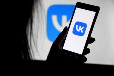 Kharkiv, Ukrayna - 20 Aralık 2021: VK ekranlı bir telefon genç bir kızın elinde bir monitörün arka planına karşı. Seçici odak.