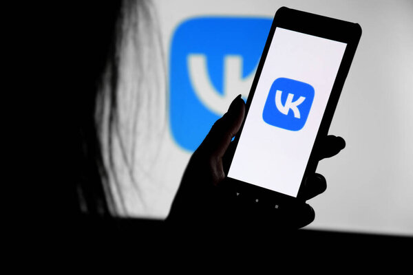 Kharkiv, Ukraine - Desember 20, 2021: A phone with a VK screen in the hands of a young girl against the background of a monitor. Selective focus.