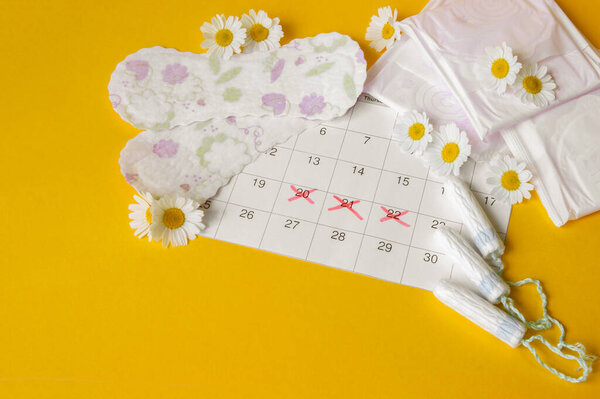 Менструальные прокладки и тампоны на календаре менструации с ромашками на желтом фоне. Концепция женского здоровья, личной гигиены в критические дни.