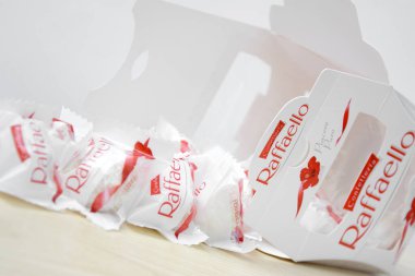 KHARKIV, UKRAINE - 23 Ekim 2021: Raffaello tatlılar açık ahşap bir masa ve beyaz zemin üzerinde. Raffaello küresel bir Hindistan cevizli badem şekerlemesidir..