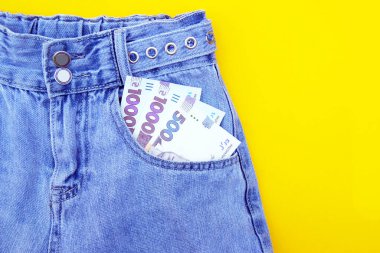 Düz yatış, sarı arka planda cebinde Ukrayna Hryvnia banknotları olan kot pantolonlar. Alışveriş ve indirim konsepti. Kara Cuma.