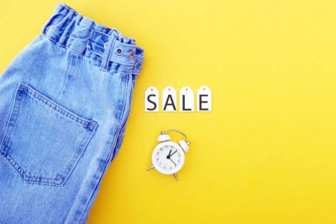 Düz yatak, kot pantolonlar, beyaz etiketler ve sarı arka planda indirimler. Alışveriş ve indirim konsepti. Kara Cuma.