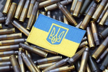 Askeri kamuflajın arka planında kabuklarla çevrili arma armalı Ukrayna ulusal bayrağı. Ukrayna 'da savaş. Savaşı durdurun..