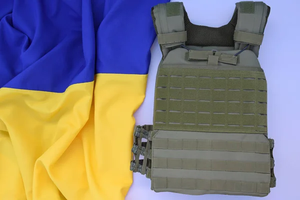 Tactical, military body armor with plates on the background of the flag of Ukraine. The concept of protecting the body from shots in the war in Ukraine.