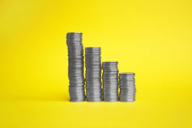 Several columns of coins on a yellow background. The concept of savings, earnings growth, economy and so on.