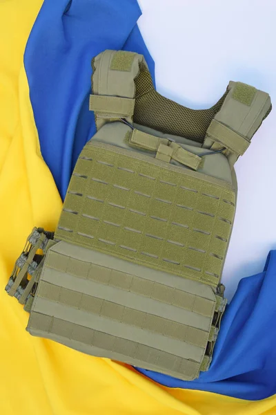 Tactical, military body armor with plates on the background of the flag of Ukraine. The concept of protecting the body from shots in the war in Ukraine.