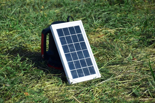 Small compact solar battery for tourism. She is charging while lying on the green grass.