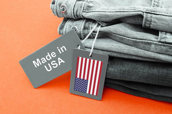 Черные джинсы, серые этикетки и надпись Made in USA на оранжевом фоне. Концепция покупки, продажи, шопинга и трикотажной современной одежды.