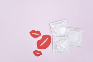 Bir sürü beyaz paket açılmamış prezervatif ve pembe arka planda kağıt öpücükler. Hamilelik veya cinsel yolla bulaşan hastalıkları azaltmak için prezervatif kullanmak. Cinsel yolla bulaşan hastalıklar. Güvenli seks ve üreme sağlığı kavramı.