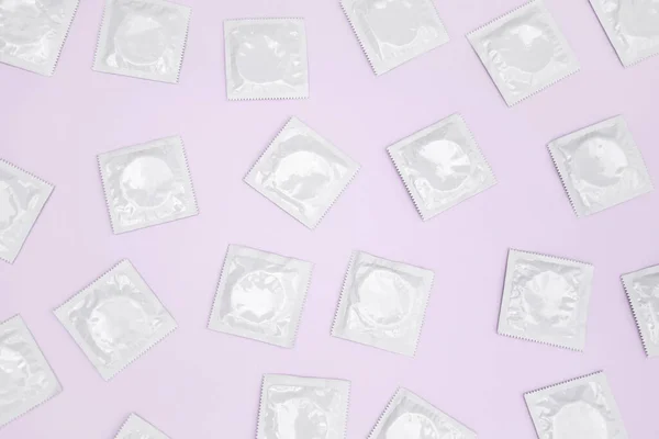Many white packages of unopened condoms on a pink background. Using a condom to reduce the chance of pregnancy or sexually transmitted diseases, STDs. The concept of safe sex and reproductive health.
